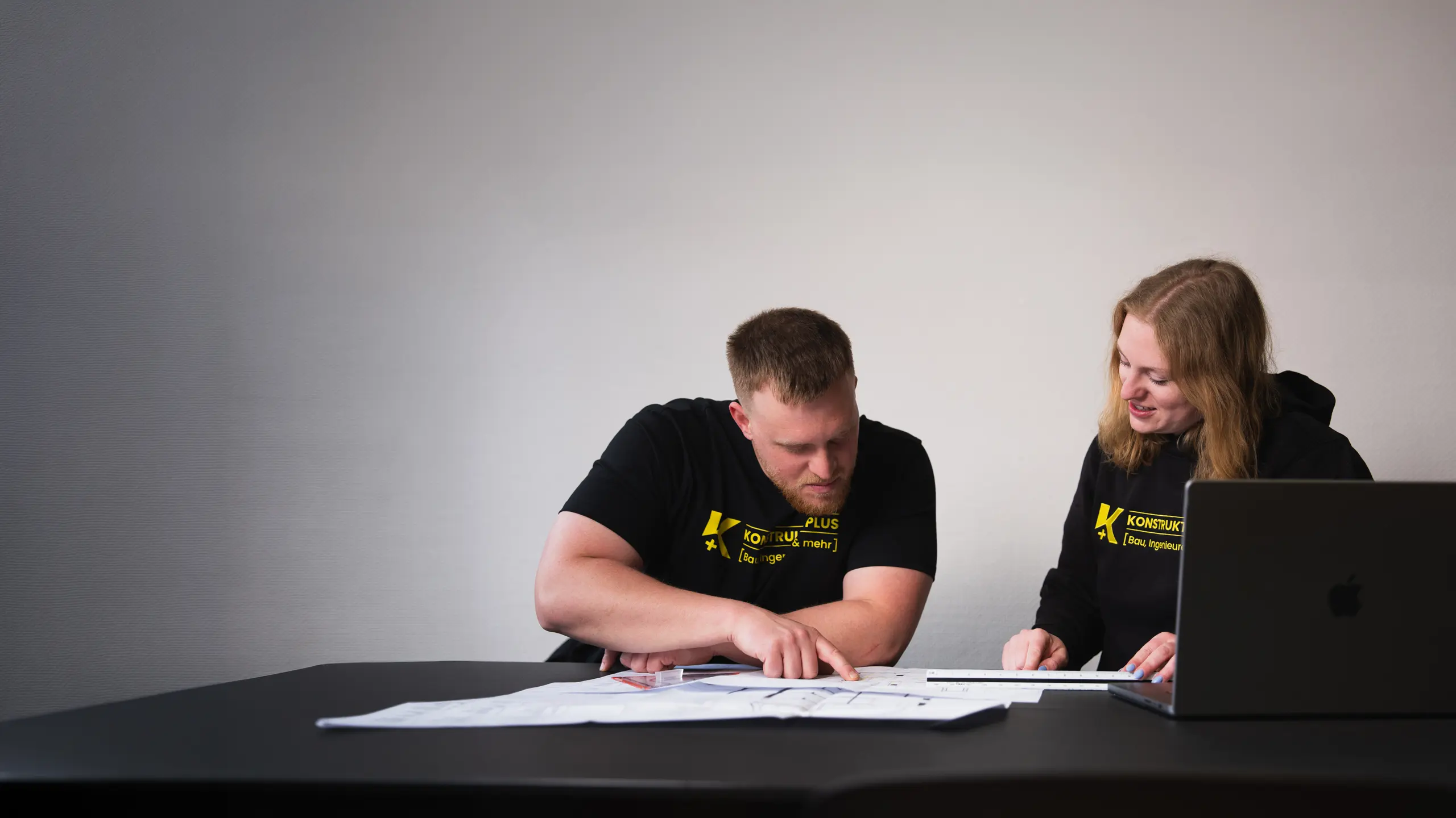 Yannick und Ronja Twistel von Konstruktiv Plus in Bielefeld besprechen gemeinsam Baupläne am Tisch, neben einem Laptop.