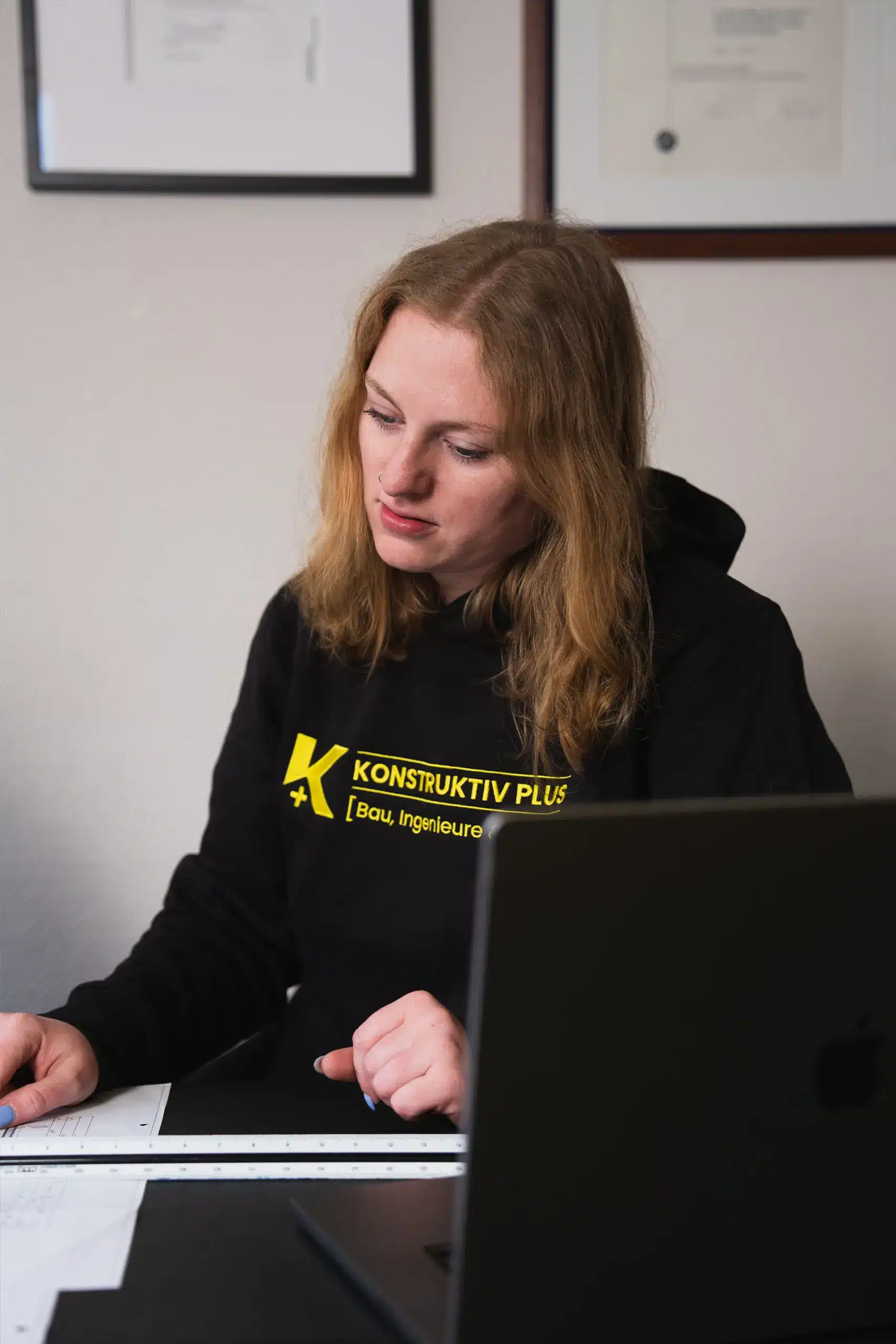 Ronja Twistel von Konstruktiv Plus in Bielefeld arbeitet an Bauzeichnungen am Schreibtisch, ein Laptop steht im Vordergrund.